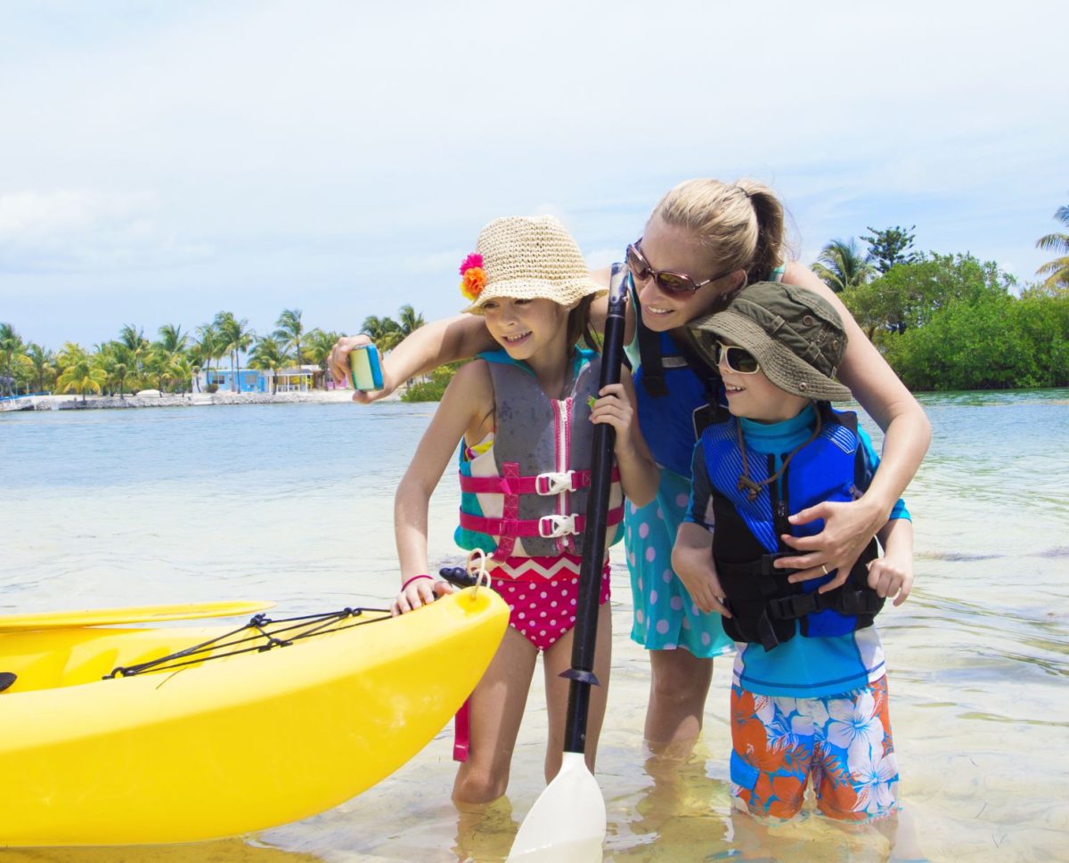 Family poses for a photo standing in the water with their yellow kayak. 