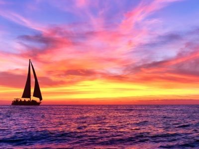 Far off sailboat with purple and orange sky.