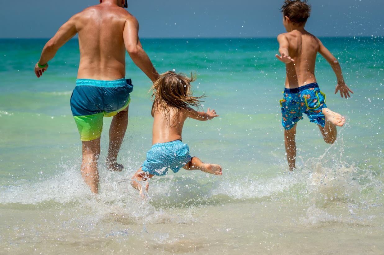 Kids & Parent Running Into Water On Beach